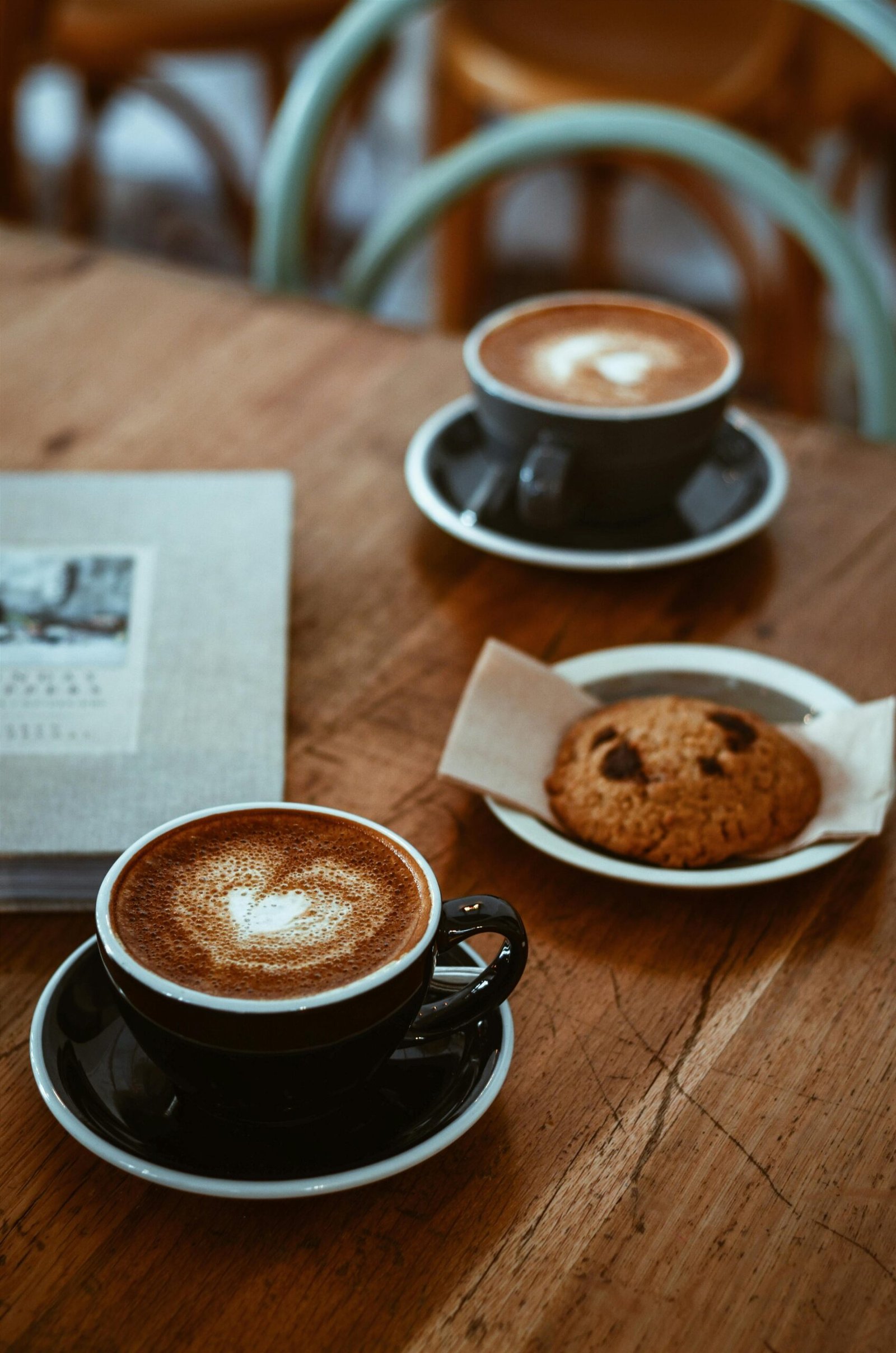 Cozy cafe setup with cappuccinos and a chocolate chip cookie on a rustic wooden table.