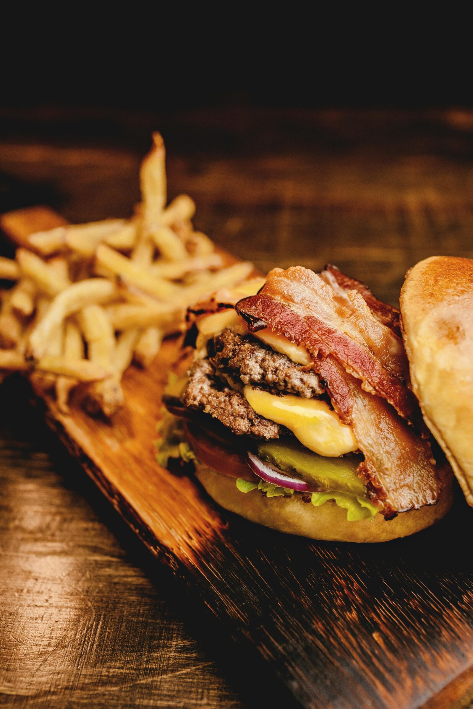 Savor a mouthwatering bacon cheeseburger with crispy fries on a rustic wooden board. Perfect fast food indulgence.